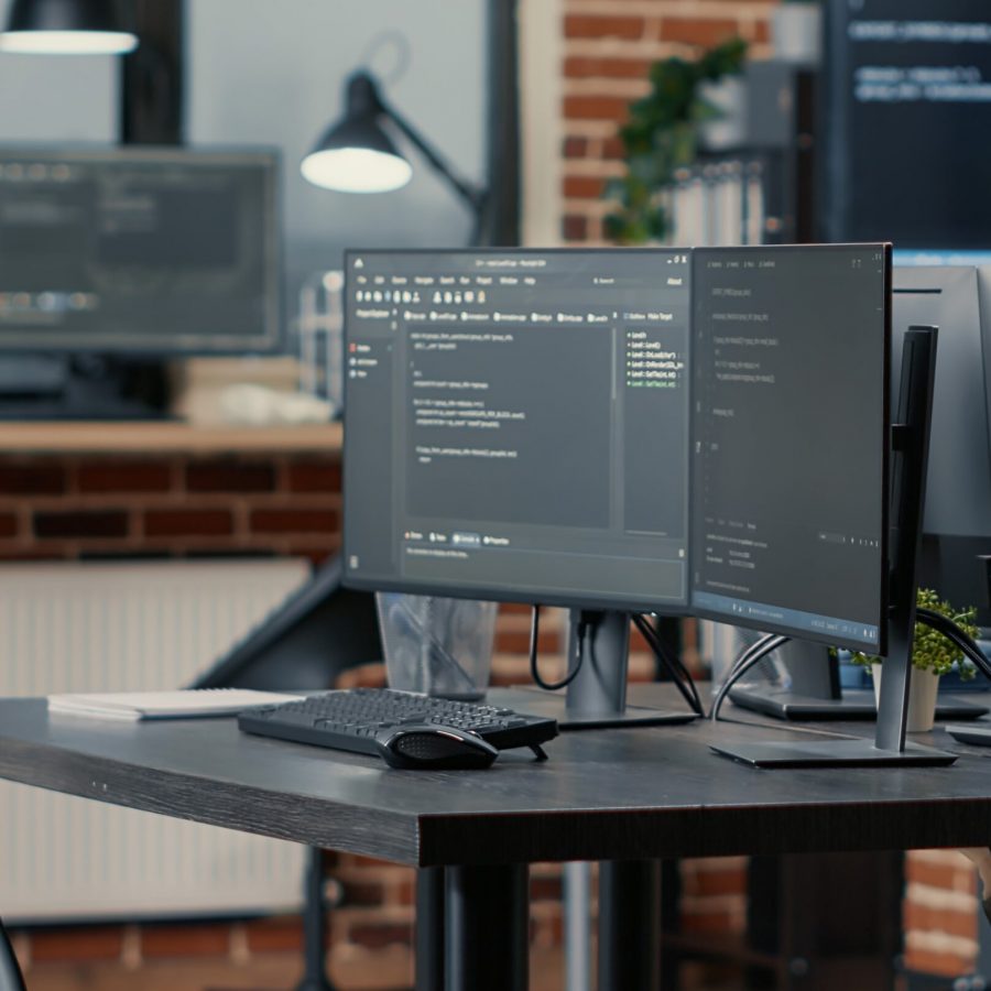 Computer screens running programming code in empty software developing agency office